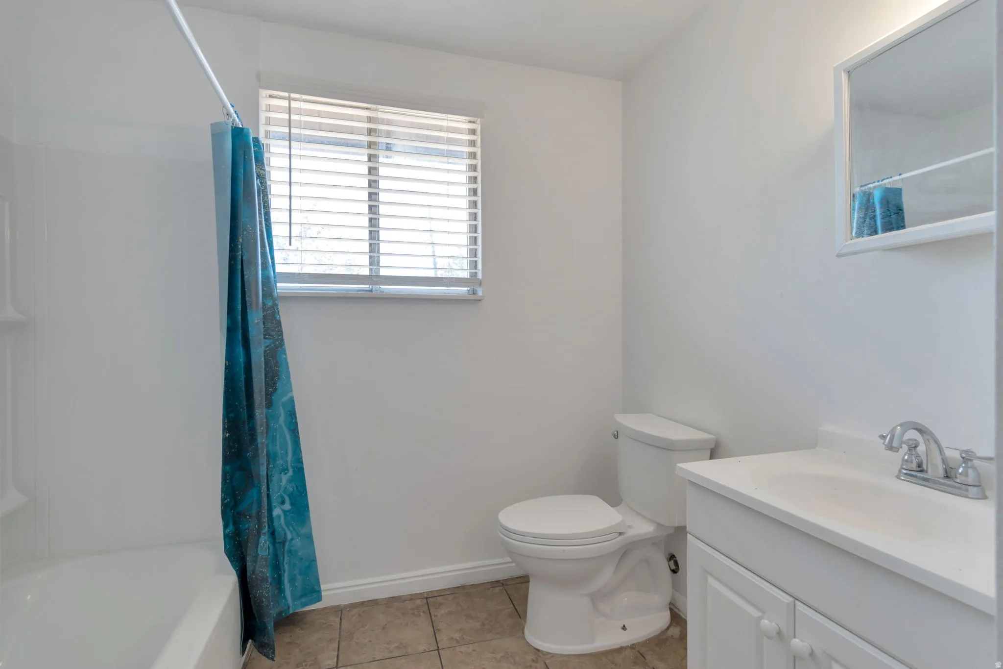 Bathroom featuring a window with blinds, a white bathtub, a toilet, a vanity with a white countertop and cabinet, and a mirrored medicine cabinet