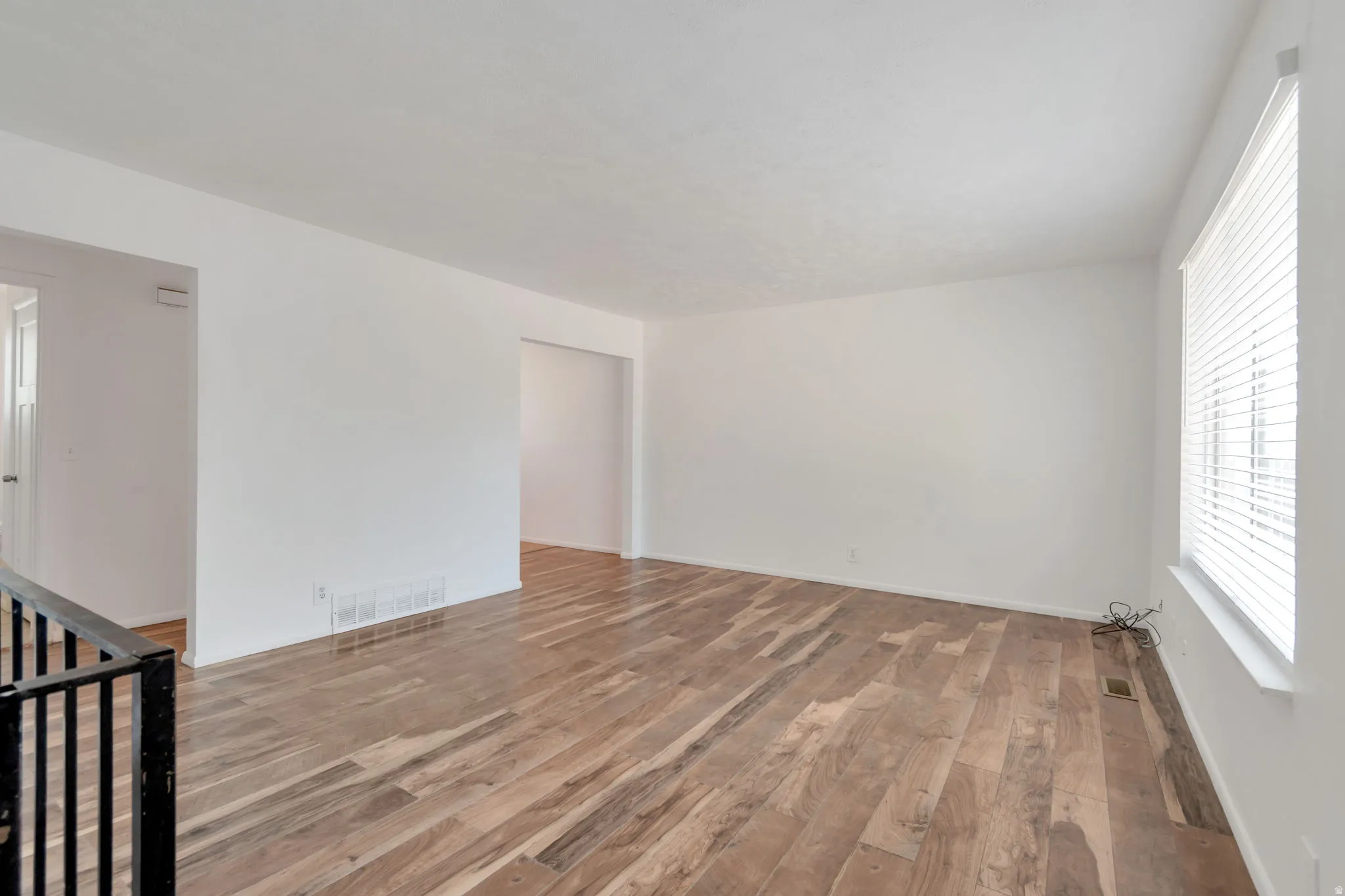 Spacious interior featuring wood-finish flooring, white walls, and a large window with horizontal blinds