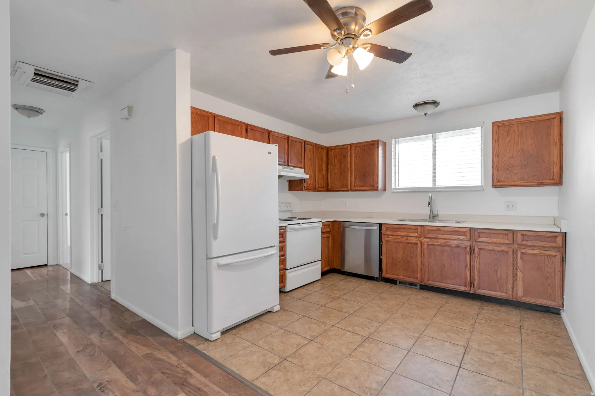Kitchen featuring wood cabinetry, light-toned countertops, a stainless steel dishwasher, and tile flooring
