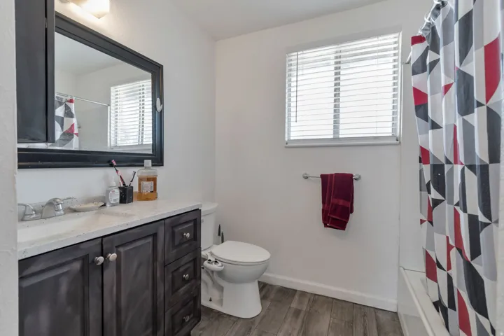 Vanity with a light-toned countertop, wood-finish flooring, a window with blinds, and a built-in bathtub
