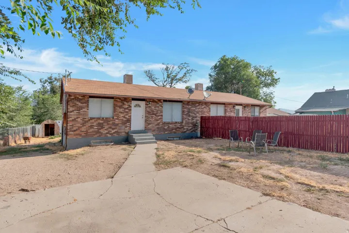 Brick exterior with a brown shingle roof, concrete pathway, and a red privacy fence
