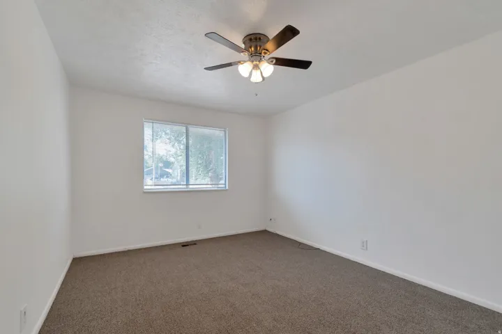 Carpeted room with a ceiling fan, light fixture, and single window