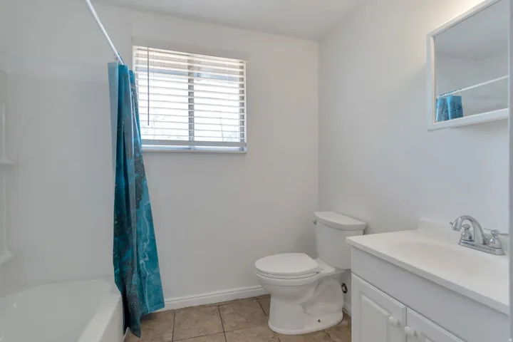 Bathroom featuring a window with blinds, a white bathtub, a toilet, a vanity with a white countertop and cabinet, and a mirrored medicine cabinet