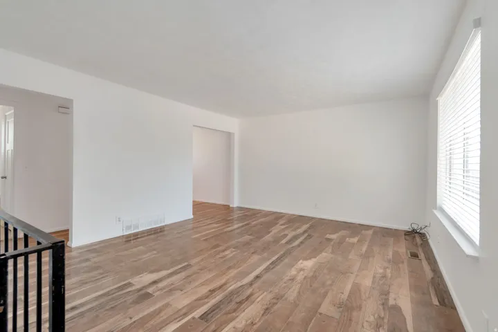 Spacious interior featuring wood-finish flooring, white walls, and a large window with horizontal blinds