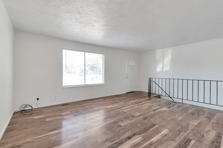 Expansive room featuring wood-finish flooring, white walls, and a large window with blinds