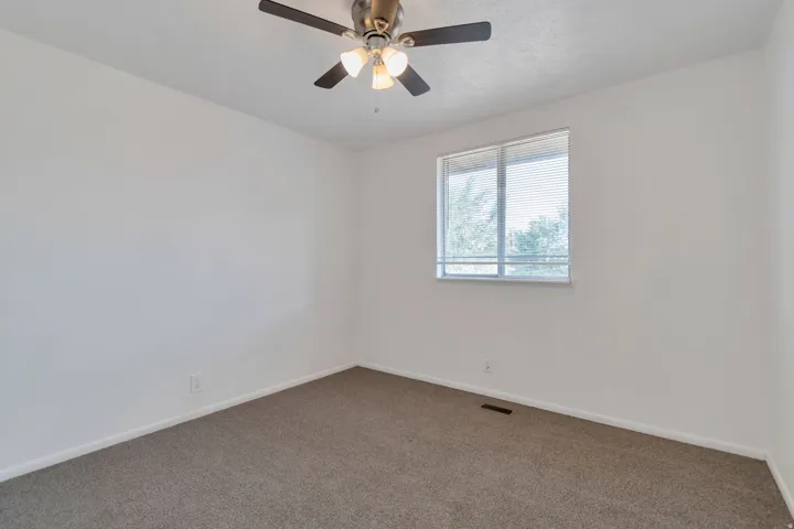 Neutral wall paint, textured carpeting, contemporary ceiling fan with lighting, and a window with horizontal blinds