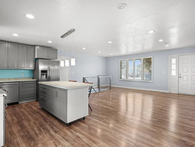 Open concept living space featuring wood-finish flooring, stainless steel appliances, a kitchen island with a light-toned countertop, recessed lighting, and a front entry door with a sidelight