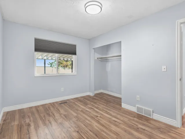 Wood-finish flooring, recessed closet space with clothing rod, ceiling-mounted light fixture, and window with exterior pergola