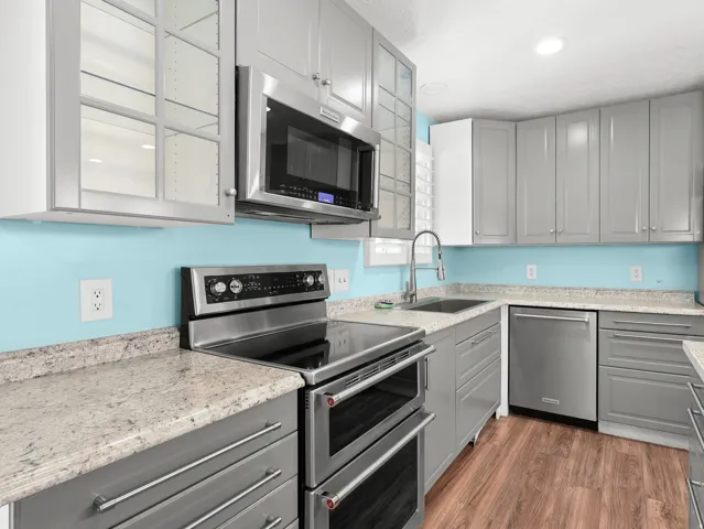 Stainless steel appliances, grey cabinetry with sleek hardware, light-toned countertops, wood-finish flooring, and recessed ceiling lighting
