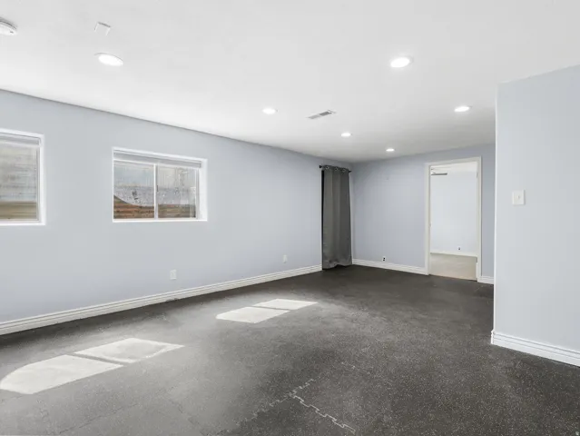Recessed lighting, light gray painted walls, two windows, dark interlocking floor tiles, and a doorway opening to another room