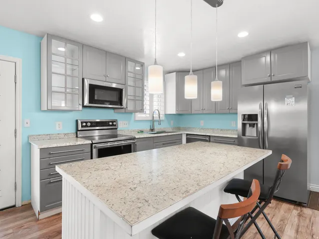 Kitchen featuring light gray cabinetry, stainless steel appliances, light-toned countertops, a center island with a breakfast bar, and wood-finish flooring