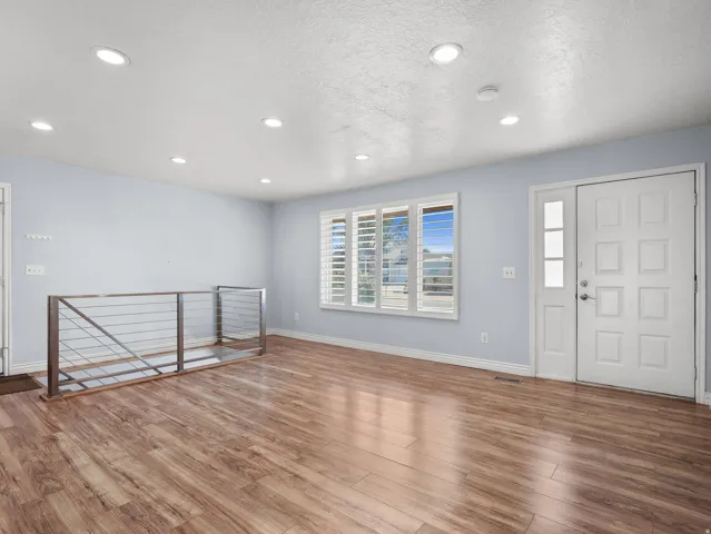 Recessed lighting, wood-finish flooring, white paneled entry door, window with plantation shutters, and a stainless steel cable railing