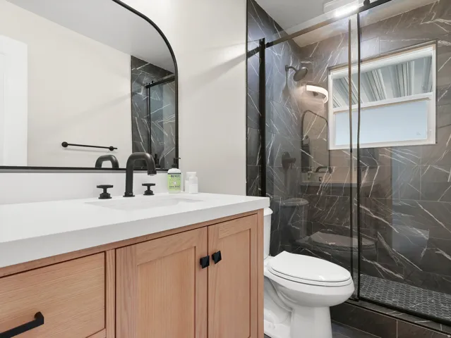 White countertop vanity with wood-finish cabinetry, black hardware, and an integrated sink with a matte black faucet