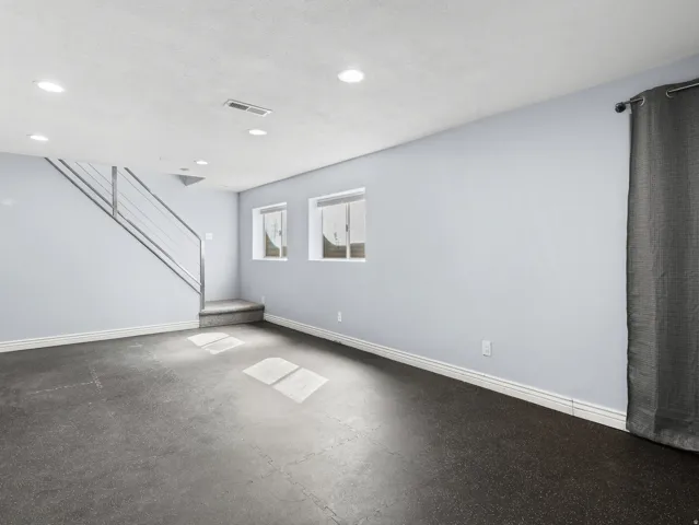 Recessed lighting, light gray wall color, dual windows, gray interlocking floor tiles, and a staircase with a metal railing