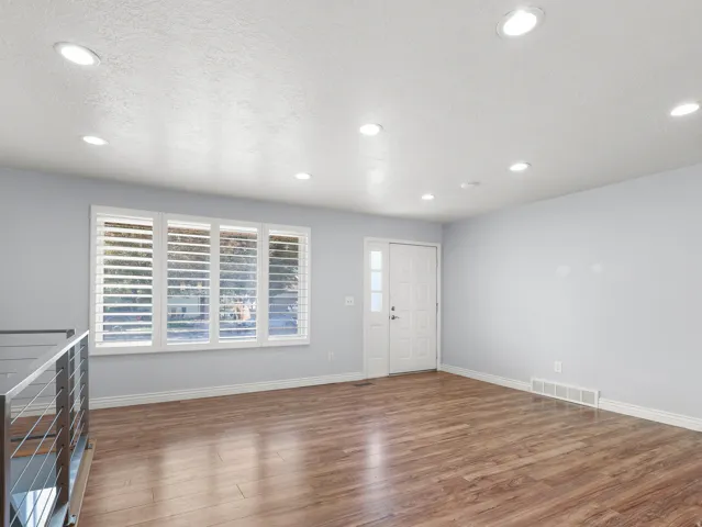 Recessed lighting, wood-finish flooring, white plantation shutters, white paneled entry door with sidelight, and a stainless steel and cable railing system