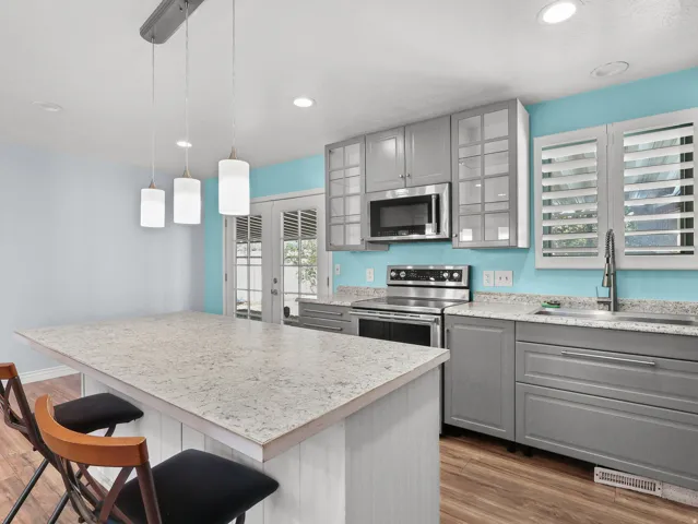 Kitchen featuring wood-finish flooring, an island with a light-colored countertop, recessed lighting, pendant lighting, and stainless steel appliances