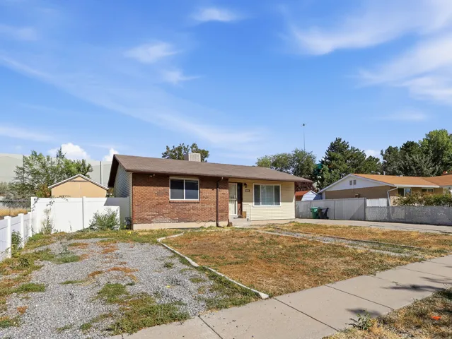Brick and siding exterior, front yard with concrete and gravel, white privacy fencing, and a side building