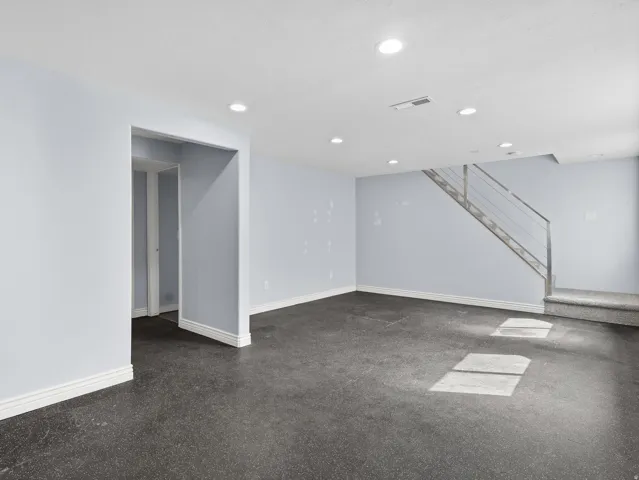 Recessed lighting, light gray walls, white trim, modern staircase with metal railings, and dark flooring