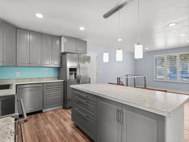 Kitchen featuring gray cabinetry, stainless steel appliances, light-toned countertops, wood-finish flooring, and recessed lighting