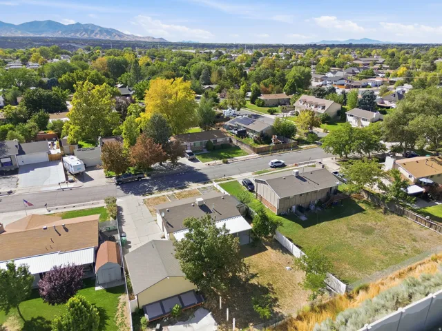 Expansive grass lot with mature perimeter trees, mountains in the distance, and established residential surroundings