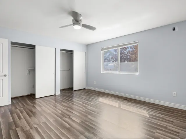 Wood-finish flooring, overhead ceiling fan with integrated lighting, window with roller shade, and two sliding closet doors
