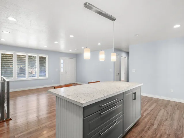 Kitchen island with a light-toned countertop and dark gray cabinetry, complemented by a linear pendant light fixture