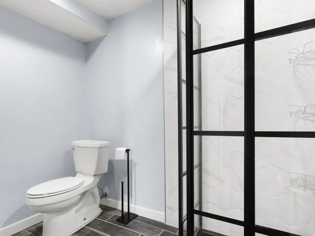 Shower enclosure with black grid frame, hexagonal tile surround, and dark wood-finish flooring