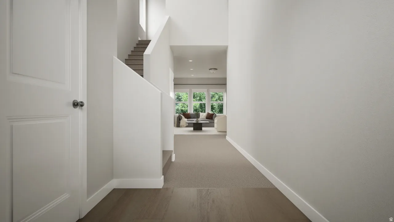 Spacious hallway with wood-finish flooring, two-panel interior door, and a carpeted staircase with white risers
