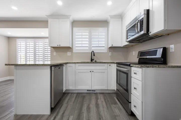 White shaker cabinetry, stainless steel appliances, granite countertops, wood-finish flooring, and plantation shutters