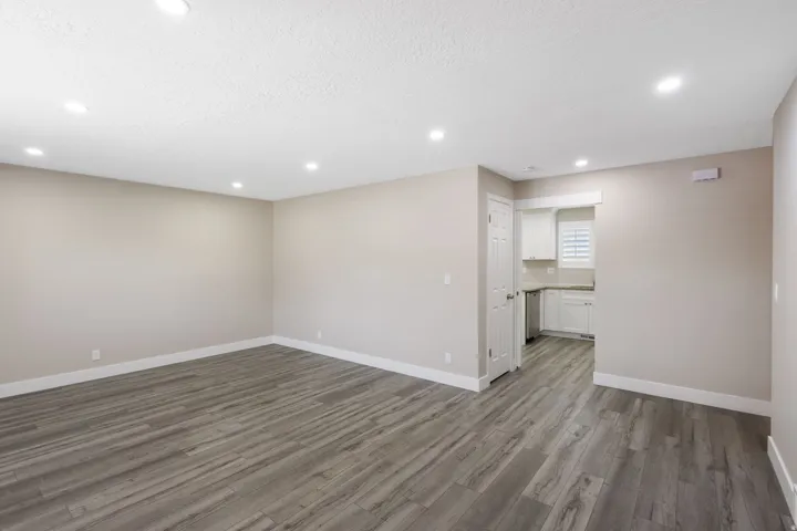 Recessed ceiling lighting, wood-finish flooring, neutral wall tones, white trim, and a white kitchen with stainless steel appliances