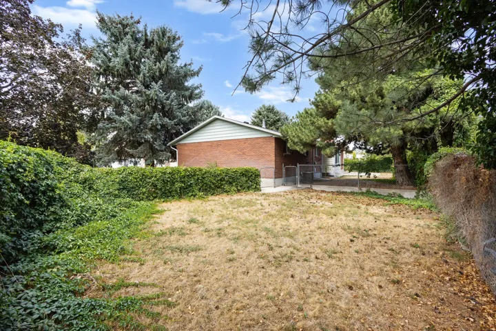 Rear exterior with brick and siding, surrounded by mature trees and a chain-link fence