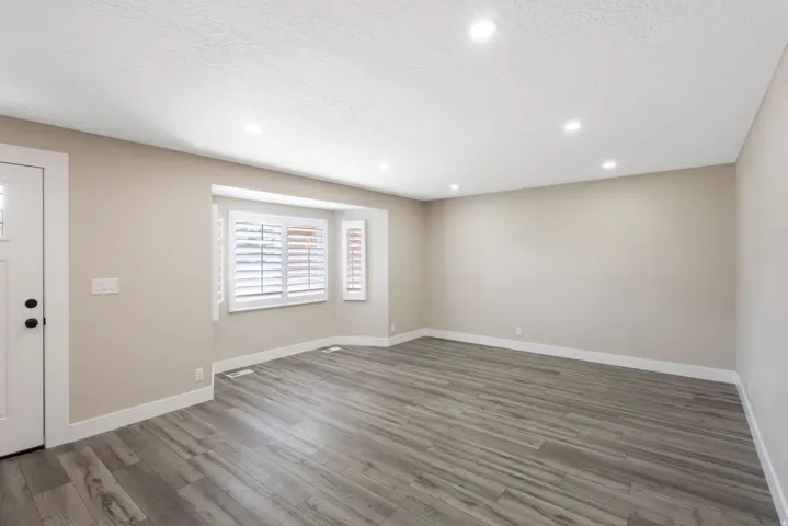 Spacious room with wood-finish flooring, recessed lighting, and a bay window featuring plantation shutters