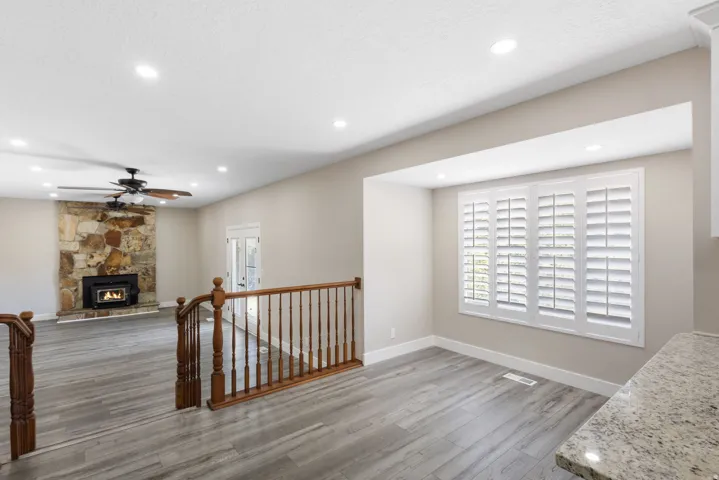 Spacious living area featuring a stone-clad fireplace with a wood-burning insert, wood-finish flooring, recessed lighting, and a ceiling fan