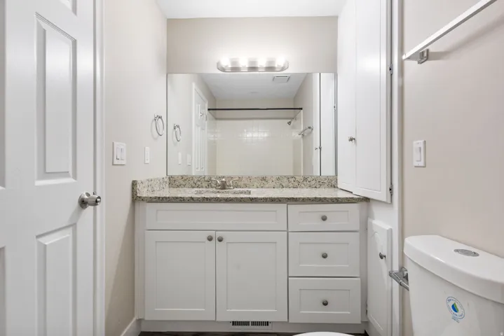 Vanity with a light-colored countertop, white cabinetry with silver hardware, large mirrored wall, and built-in vertical storage