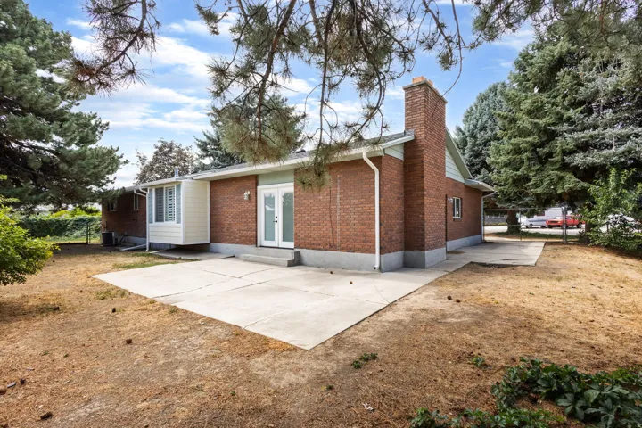 Brick exterior with an integrated chimney, concrete patio, white French doors, and mature perimeter trees