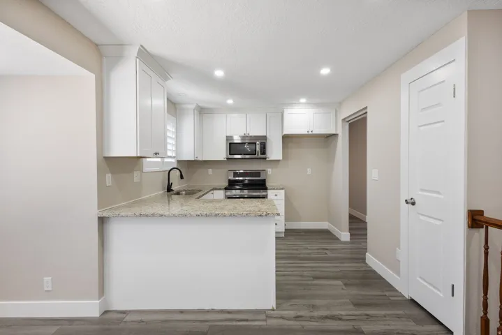 Kitchen featuring white cabinetry, light-toned countertops, stainless steel appliances, and wood-finish flooring