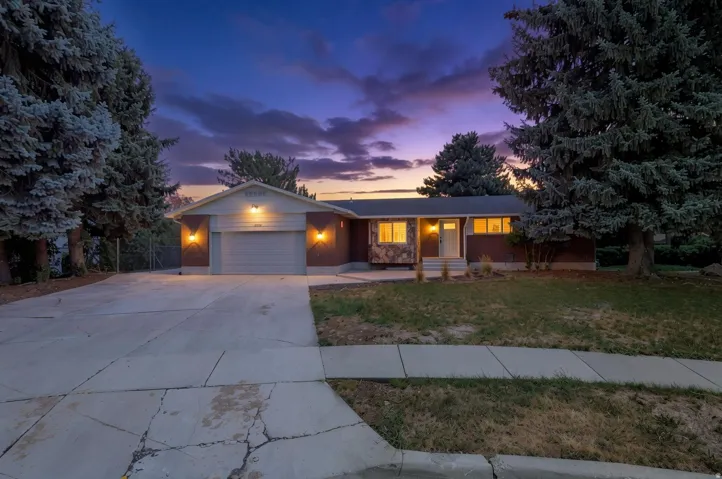Exterior featuring a stone facade, attached garage, concrete driveway, and mature landscaping
