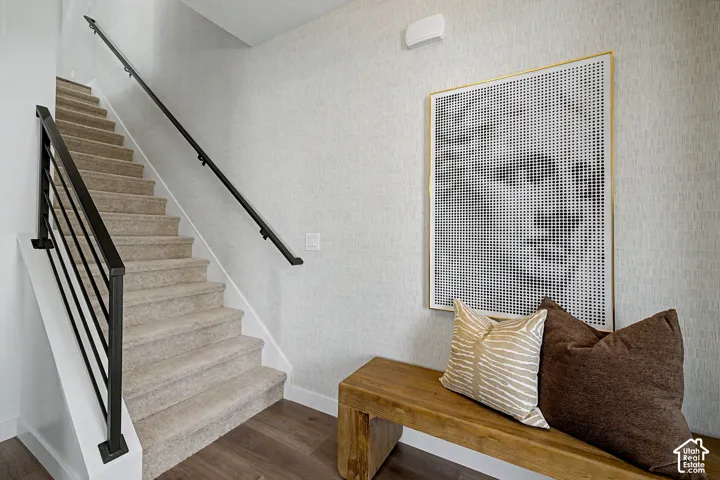 Staircase with carpeted treads, contemporary black iron balusters, black handrail, and textured wall covering