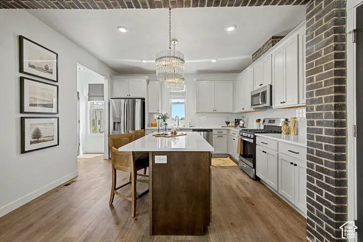 Open-concept kitchen with wood-finish flooring, white cabinetry, stainless steel appliances, a center island with seating, and recessed lighting