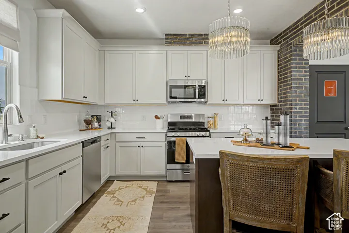 Modern kitchen featuring white shaker cabinetry, stainless steel appliances, white subway tile backsplash, and wood-finish flooring