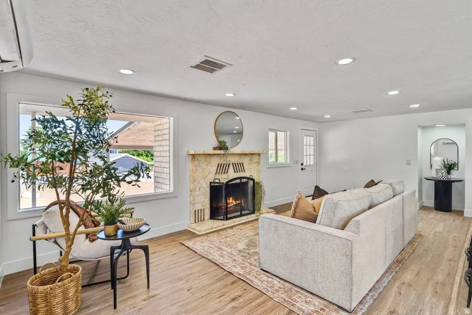 Living area with a stone-clad fireplace and hearth, wood-finish flooring, recessed lighting, and a white paneled door