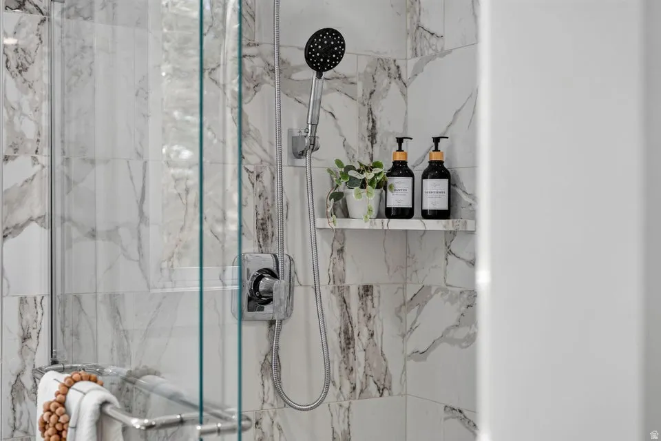 Shower with marble-look tile surround, glass enclosure, and a built-in recessed shelf