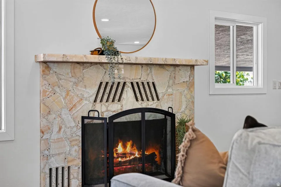 Stone surround fireplace with a metal screen and mantel, accompanied by a white-framed window