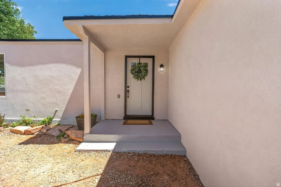 Smooth stucco exterior, covered entry, black-framed entry door with light-colored panels, and exterior sconce lighting
