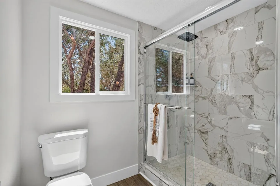 Walk-in shower with clear glass enclosure, large format marbled tile, hexagonal tile shower pan, and rainfall shower head