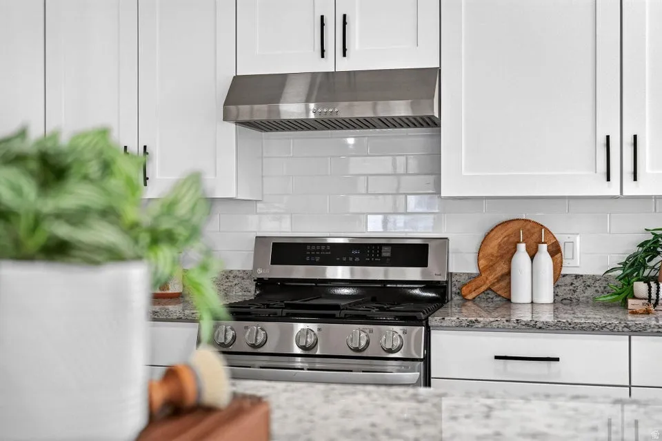 White shaker cabinetry with matte black hardware, stainless steel range with matching hood, subway tile backsplash, and granite countertops