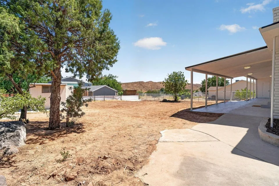Expansive outdoor patio with a covered overhang, supported by multiple columns, offering direct access to a large open lot