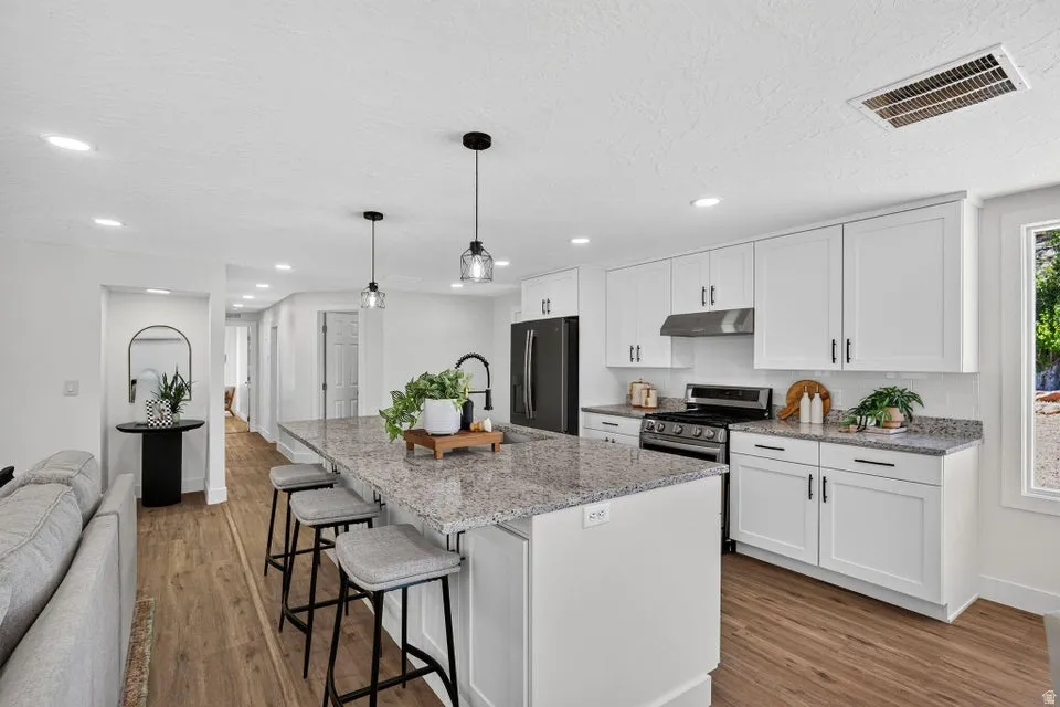 Open-concept kitchen featuring white shaker cabinetry, granite countertops, a center island with seating, and wood-finish flooring