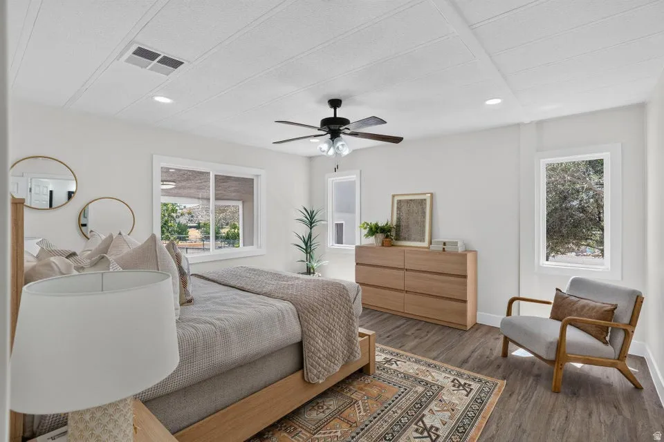 Recessed lighting, ceiling fan, multiple windows, wood-finish flooring, and a light wood-tone dresser