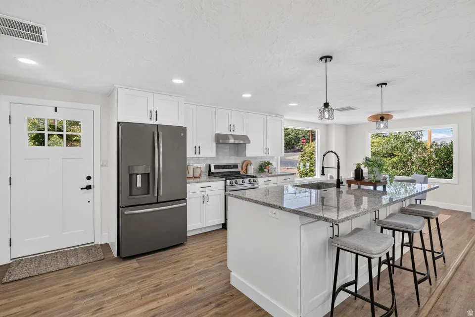Kitchen featuring a large island with seating, granite countertops, white shaker cabinetry, wood-finish flooring, and a stainless steel range
